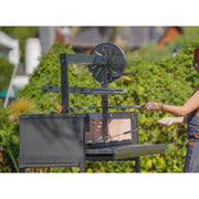 Person using a nuke puma outdoor grill with a green hedge in the background