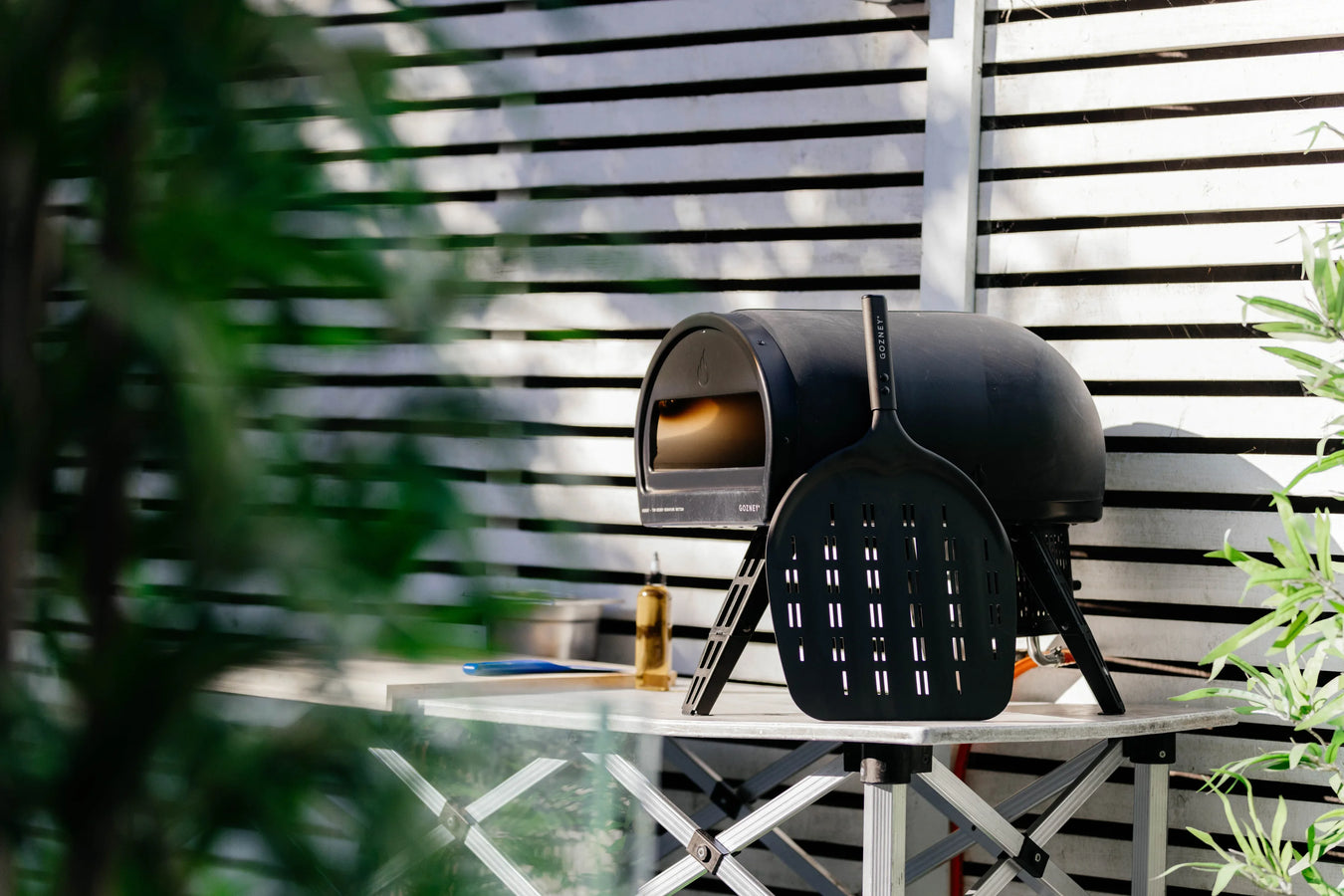 Black outdoor pizza oven on a white table with plants in the foreground